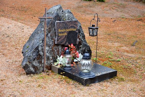 Muualle haudattujen muistokivi, risti, kynttilöitä ja kukkia