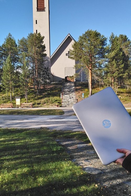Etualalla tietokone ja taustalla kivinen kirkko
